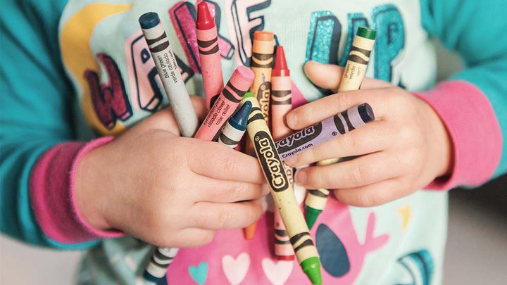 A toddler holding lots of colourful crayons