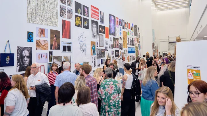 Crowd viewing artwork displayed on gallery walls at an art exhibition. Art by students from The Manchester College.