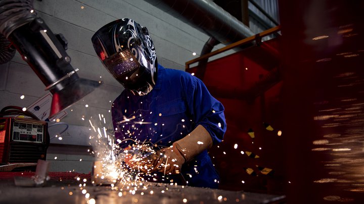 A student is welding in the engineering workshop. They are wearing a welding mask and sparks can be seen.