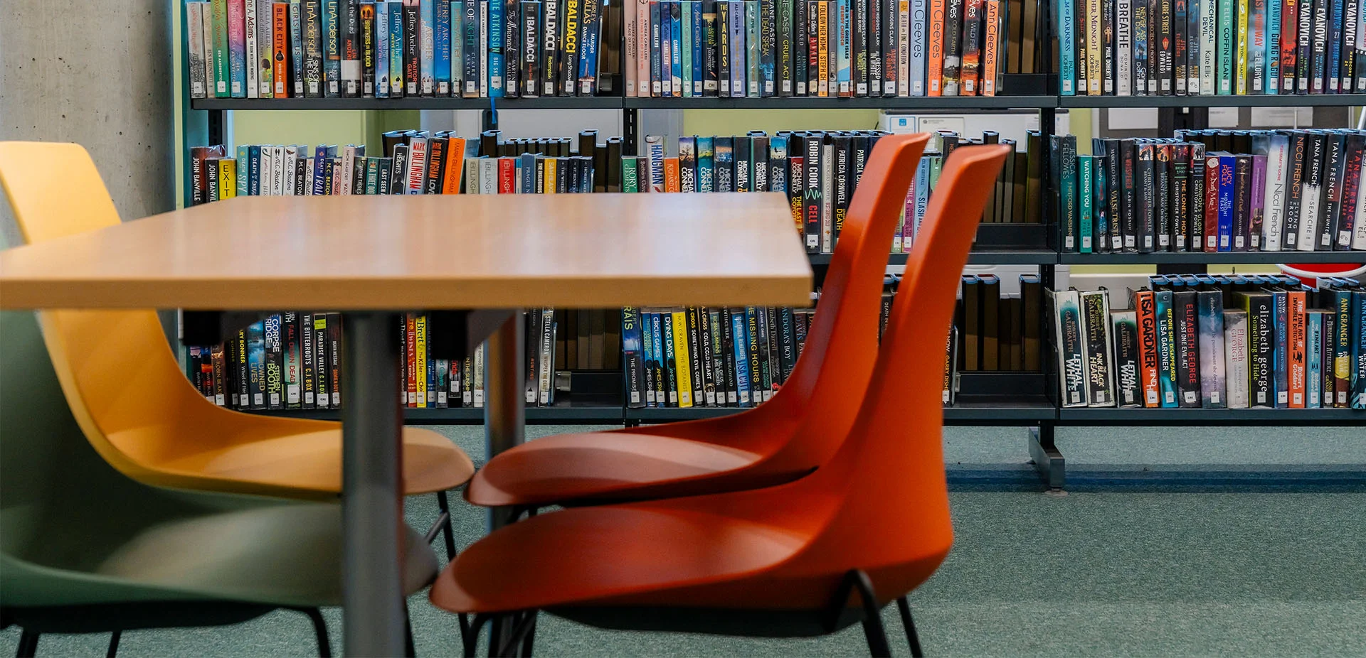 Library study area with bookshelves filled with books and a table with colourful chairs arranged for reading and independent study.