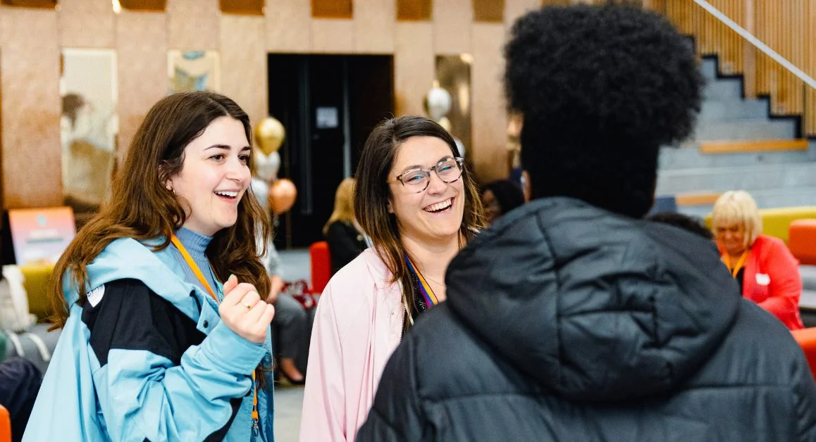A group of learners talking together in a large indoor social space at The Manchester College with balloons and modern seating behind them.