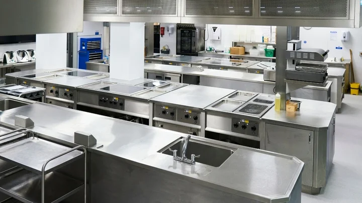 A professional training kitchen with stainless steel workstations, sinks, ovens, and food preparation areas.