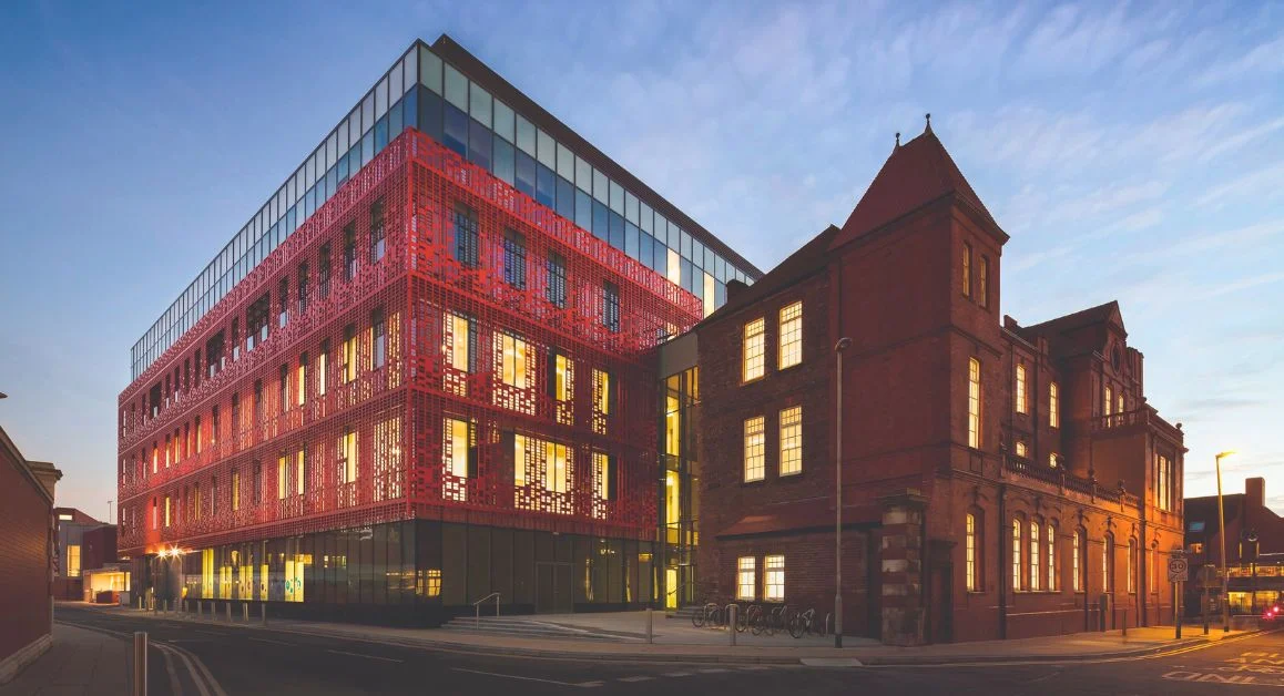 Exterior of The Manchester College City Labs Campus featuring a modern building with a red patterned facade connected to a historic brick building.