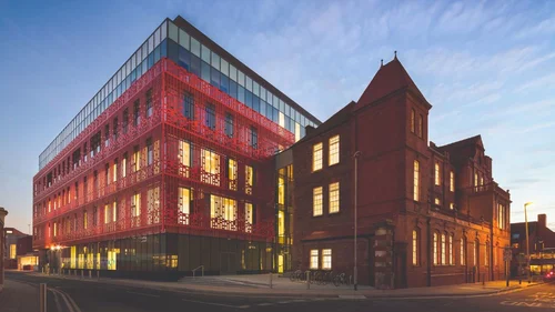 Exterior of The Manchester College City Labs Campus featuring a modern building with a red patterned facade connected to a historic brick building.