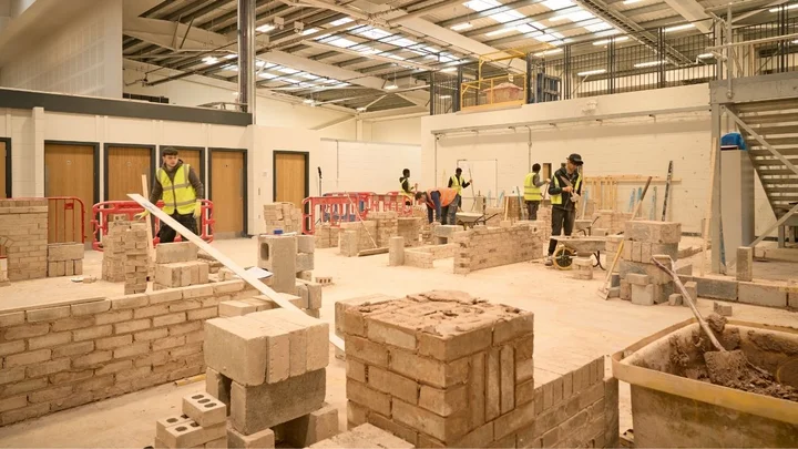 A bricklaying workshop with multiple learners building practice walls, using tools and materials across a spacious construction training environment.