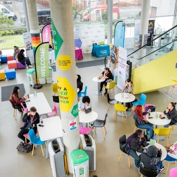 Student atrium at The Manchester College Harpurhey Campus with colourful seating, tables, open social space and staircase in a bright modern interior.