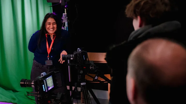 Students filming a scene in a media studio, using professional cameras and lighting equipment in front of a green screen during a creative and digital media session.