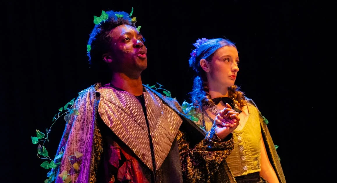 Two performing arts learners wearing stage costumes on a dark theatre set with dramatic lighting at The Manchester College.