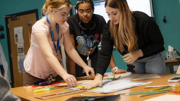 Group of people working together on a table activity, arranging maps and coloured pens during a Public Services classroom task.