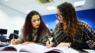 Photograph of two Business and Professional students looking at text books in a classroom setting.