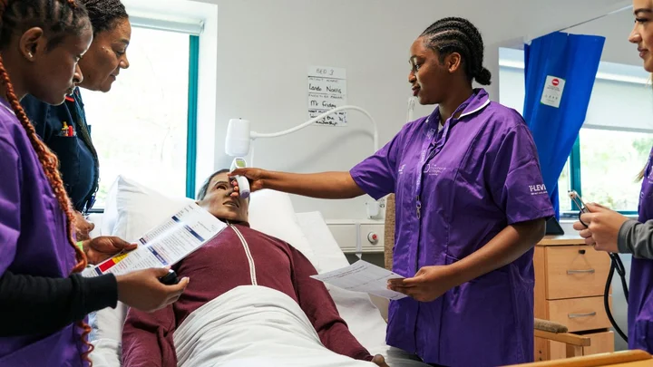 Health and Social Care students practising patient assessment skills using a healthcare simulation mannequin in a mock hospital ward at The Manchester College.
