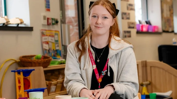A learner in an early years education classroom sitting at a play table with colourful cups and toys, participating in a practical activity related to childcare and child development.