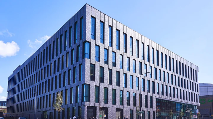 Exterior view of The Manchester College City Campus Manchester, showing a large modern building with patterned brickwork and tall vertical windows on a city street.