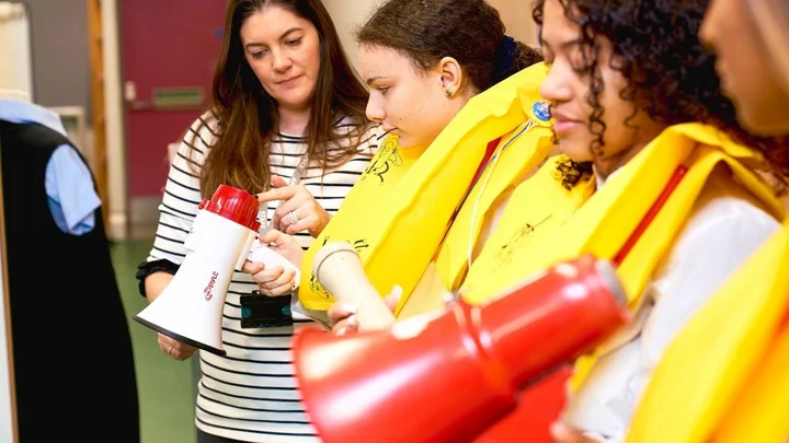 Cabin crew trainees practising emergency procedures, using megaphones while wearing life jackets during aviation safety training.