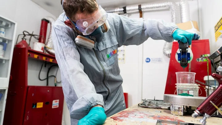 Automotive learner mixing vehicle paint while wearing full protective equipment during a practical spray preparation task.