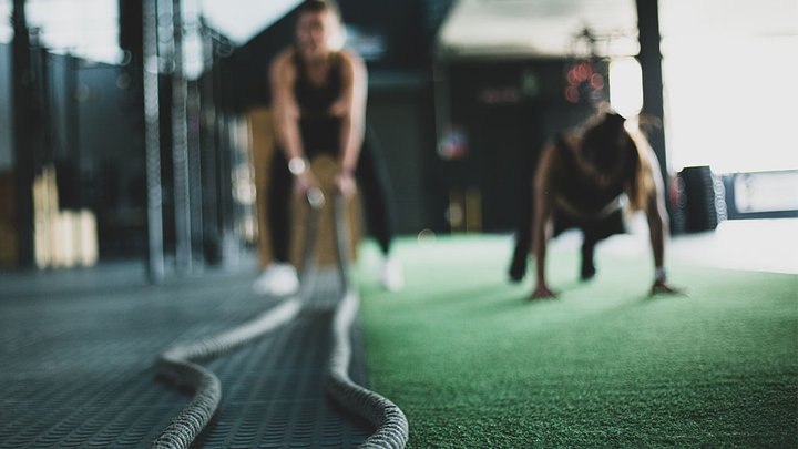 On woman doing burpees while another is on battle ropes