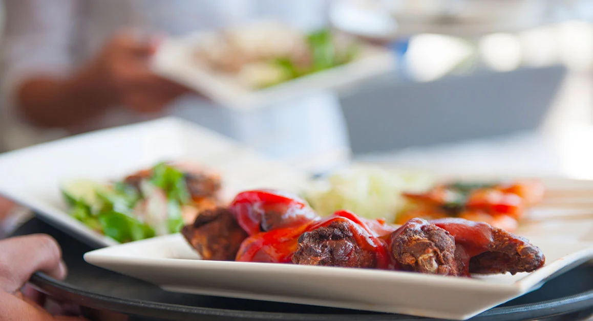 Plate of prepared food on a plate, with salad and additional meal trays blurred in the background.