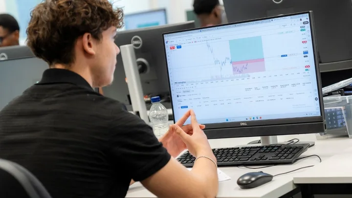 Learning space showing a person using a desktop computer to analyse financial data on screen during a practical business studies session.