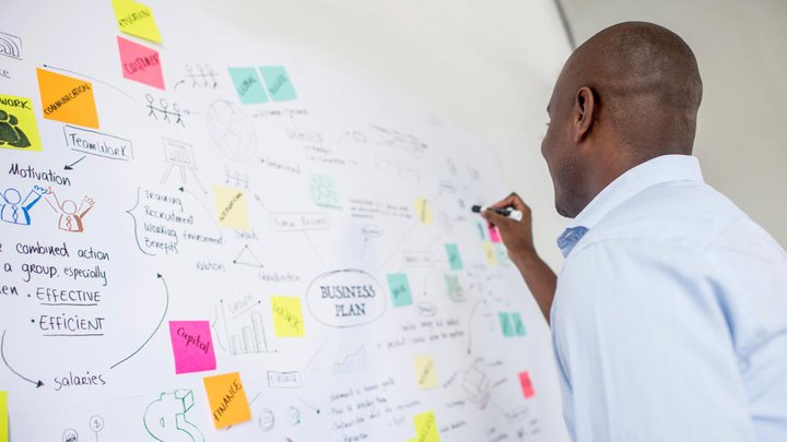 A man writing an organised, strategic business plan on a whiteboard