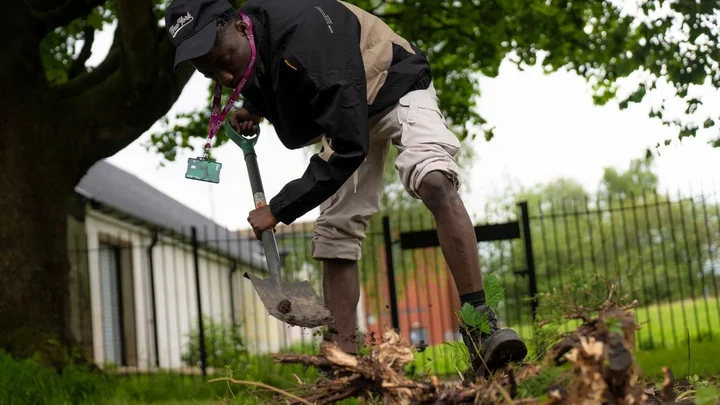 A learner using a shovel to break up and move branches during an outdoor foundation learning activity.