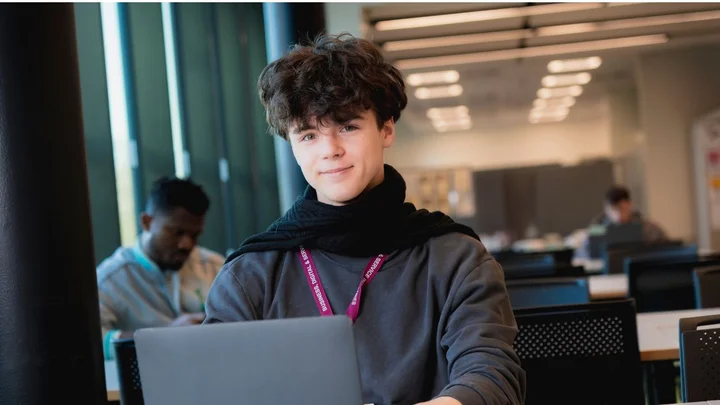 Student smiling and working on a laptop in a modern computing classroom at The Manchester College