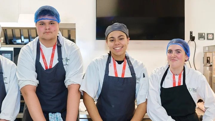 Catering students wearing chef whites and aprons standing together in a professional training kitchen.