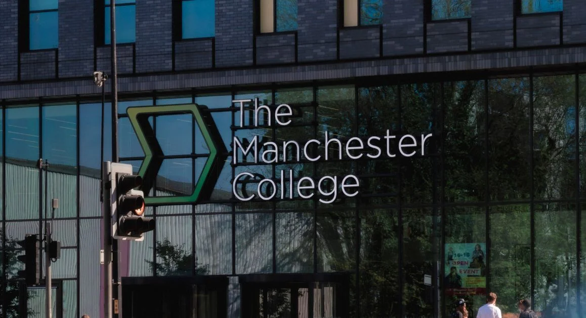 The front entrance of The Manchester College building, featuring large glass windows with the college logo displayed.