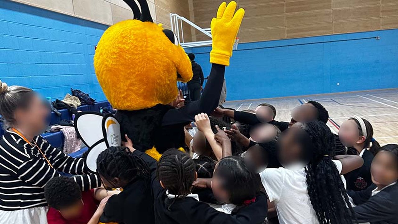 Photograph of pupils from St Francis RC Primary School hugging The Manchester College's mascot in the Sports Hall.