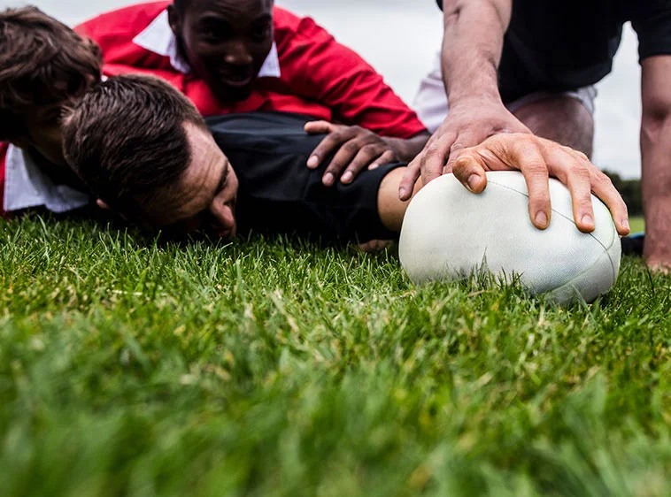 Players competing for possession of a rugby ball on a grass field.