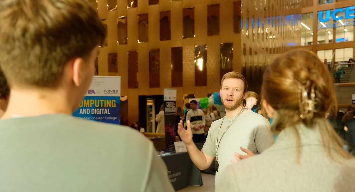 A representative from The Manchester College talking to prospective learners and their parents at an open event inside a modern college campus.