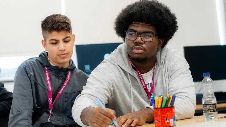Business learners working together at a desk, taking notes and discussing ideas during a classroom‑based learning session.