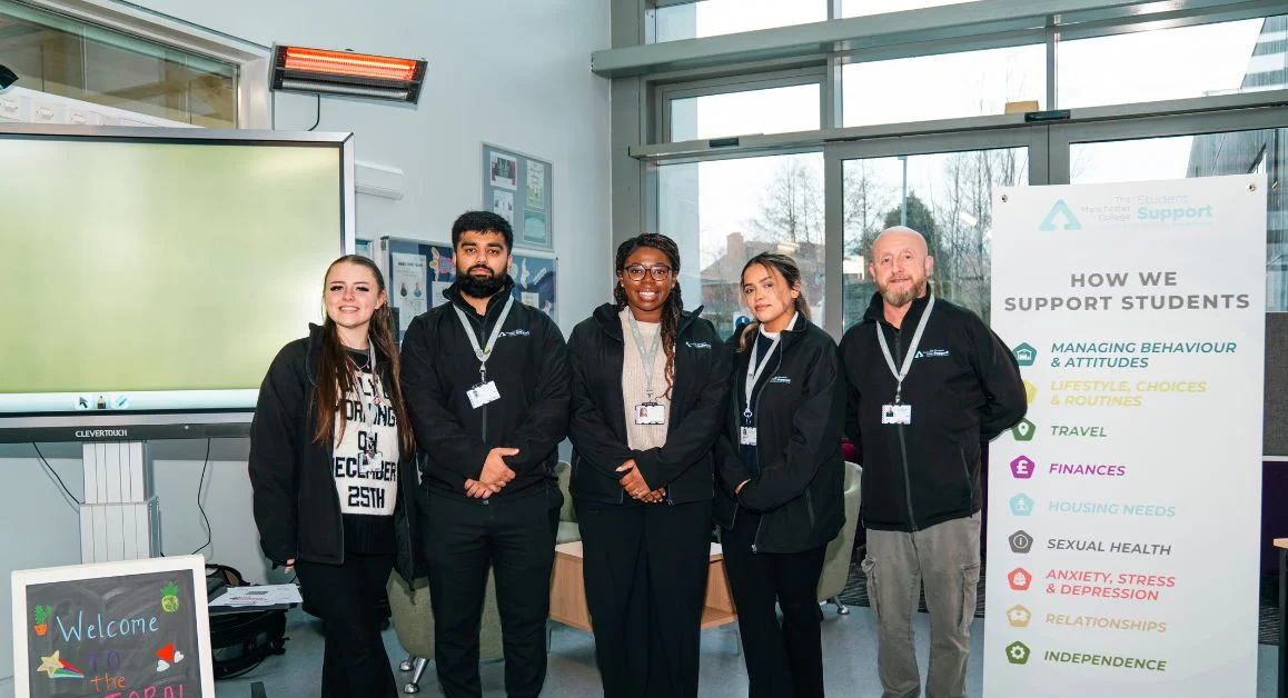 A support team standing together beside a banner outlining how The Manchester College supports students, with a large screen and reception area behind.