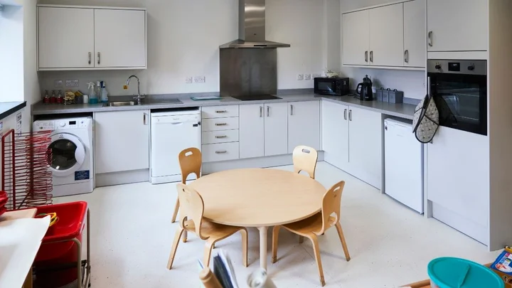 A fully equipped early years training kitchen featuring child‑sized tables and chairs, modern appliances, storage cabinets, and learning resources used for practical childcare and education sessions.