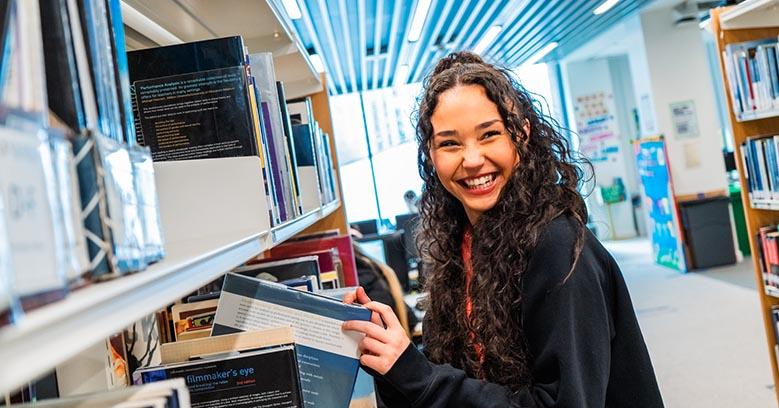 A student from The Manchester College pulling a book from a shelf in one of the College's libraries.