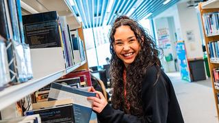 A student from The Manchester College pulling a book from a shelf in one of the College's libraries.