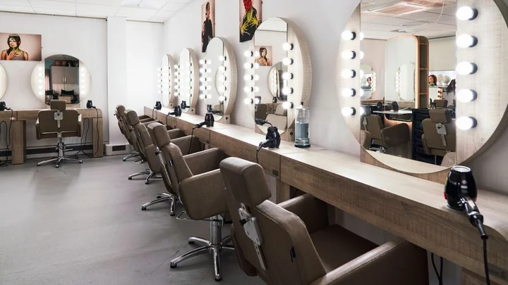 A makeup studio with illuminated mirrors, styling stations, and salon chairs arranged in a professional training environment.