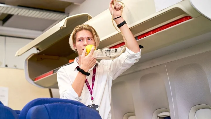A cabin crew trainee demonstrating how to use an oxygen mask during an in‑flight safety training session.