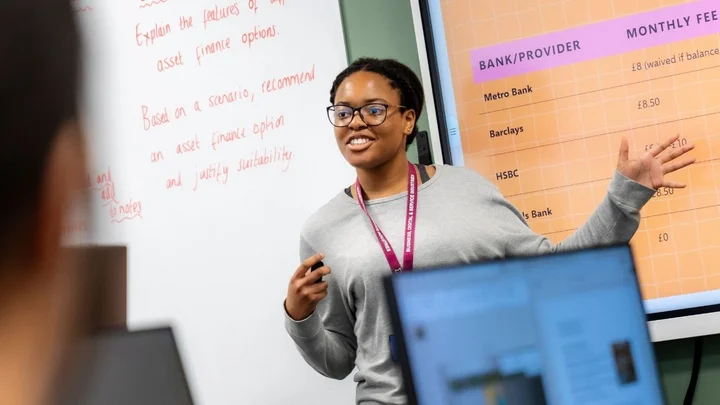 Business and Professional Services classroom showing a person delivering a presentation using a digital screen while learners work on laptops.