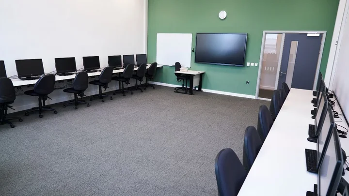 Computing and Digital classroom featuring rows of desktop computers, adjustable chairs, and an interactive display screen.