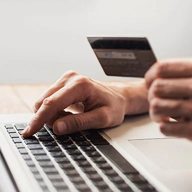Person entering payment details on a laptop while holding a bank card.