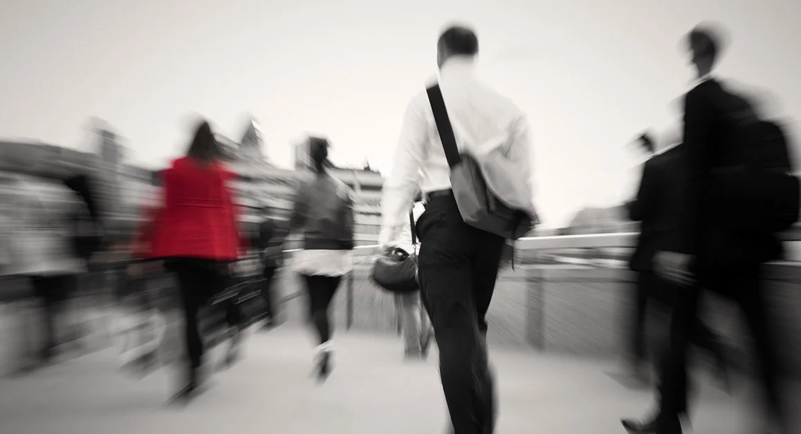 Blurred pedestrians walking in a city, with one person wearing a satchel standing out.