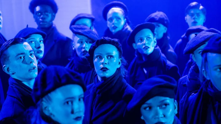 Group of performers on stage, all wearing berets, under blue lighting during a performing arts production at The Manchester College.