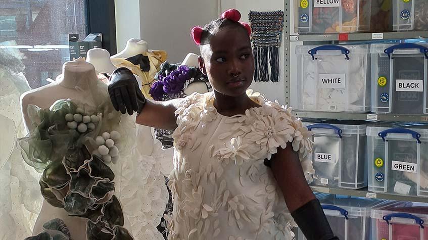 A student in a white Balenciaga dress is leaning on a mannequin and posing for an out-of-shot photographer.
