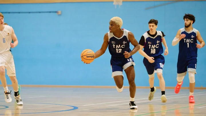 Basketball players in The Manchester College kit practicing in an indoor sports hall