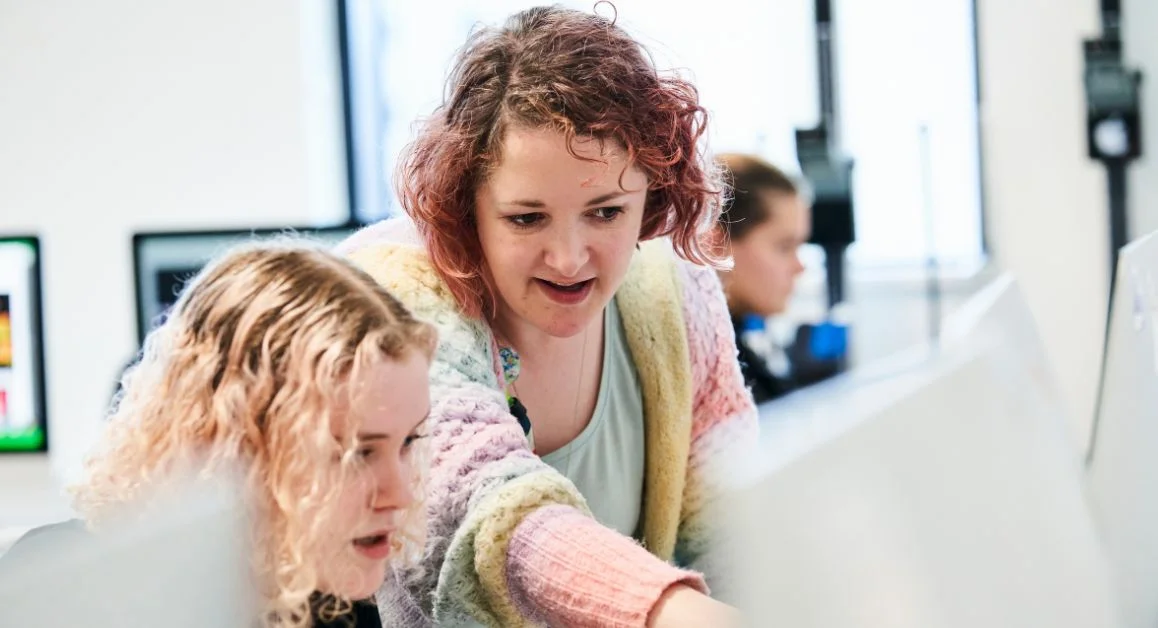 Tutor from The Manchester College supporting learners working on computers in a classroom environment.