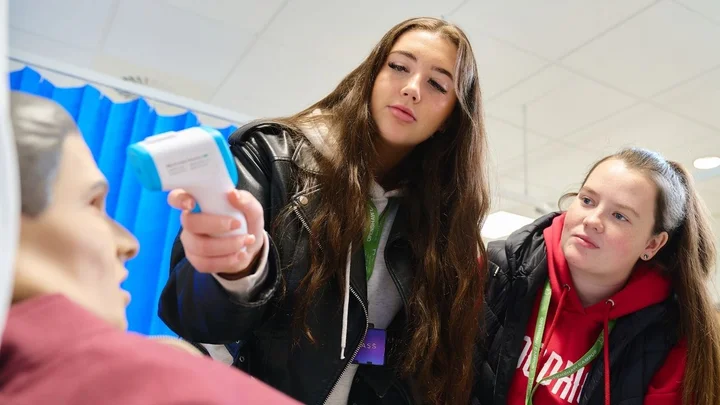 A health and social care learner using a digital thermometer during a practical clinical skills session.