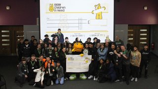 A large group of Public Services students are posing for a picture around a bee mascot, who is holding a big cheque for Children in Need.