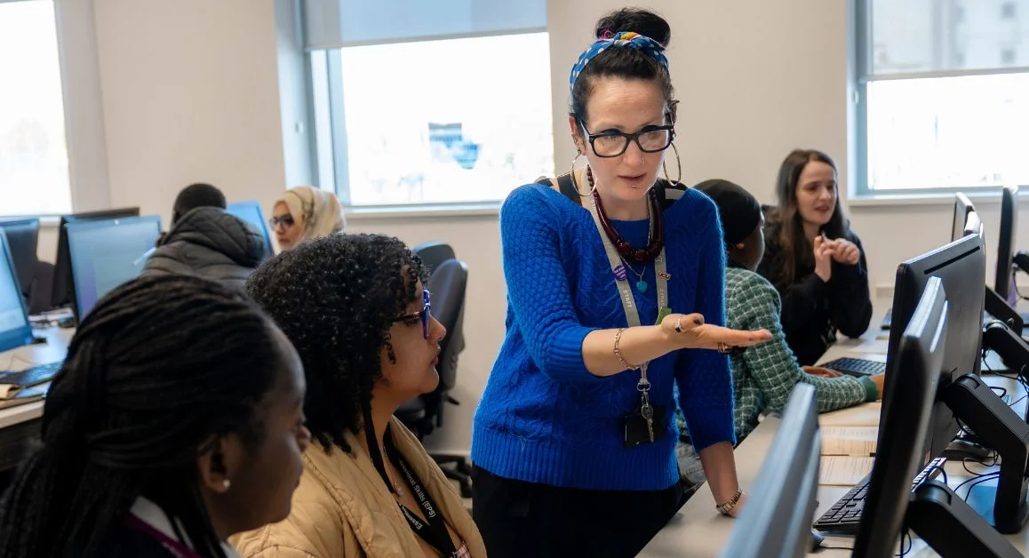 Adult students using computers in a classroom while receiving one-to-one support from a member of staff at The Manchester College.