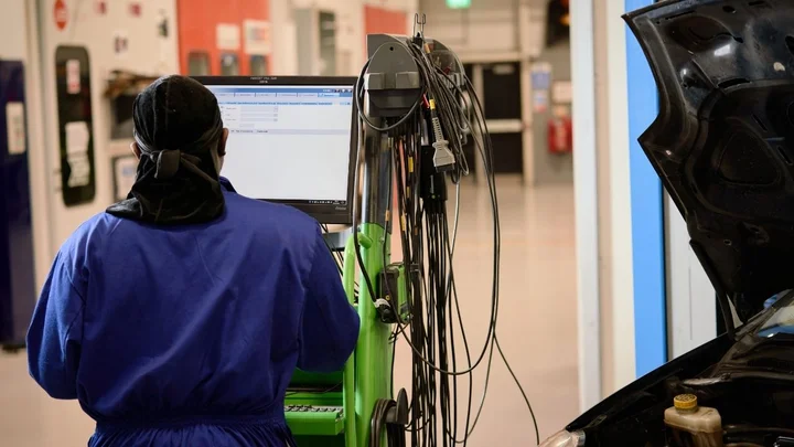 Automotive workshop facility showing a learner using a vehicle diagnostic machine connected to a car during practical automotive training.