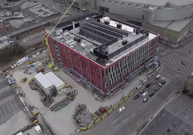 Aerial view of The Manchester College City Campus building under construction, surrounded by cranes, construction equipment and nearby city streets.